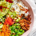 A vegan sushi bowl with rice, vegan shredded duck, edamame beans, carrot, cucumber, avocado, pink pickled ginger, sesame seeds, spring onions and hoisin sauce