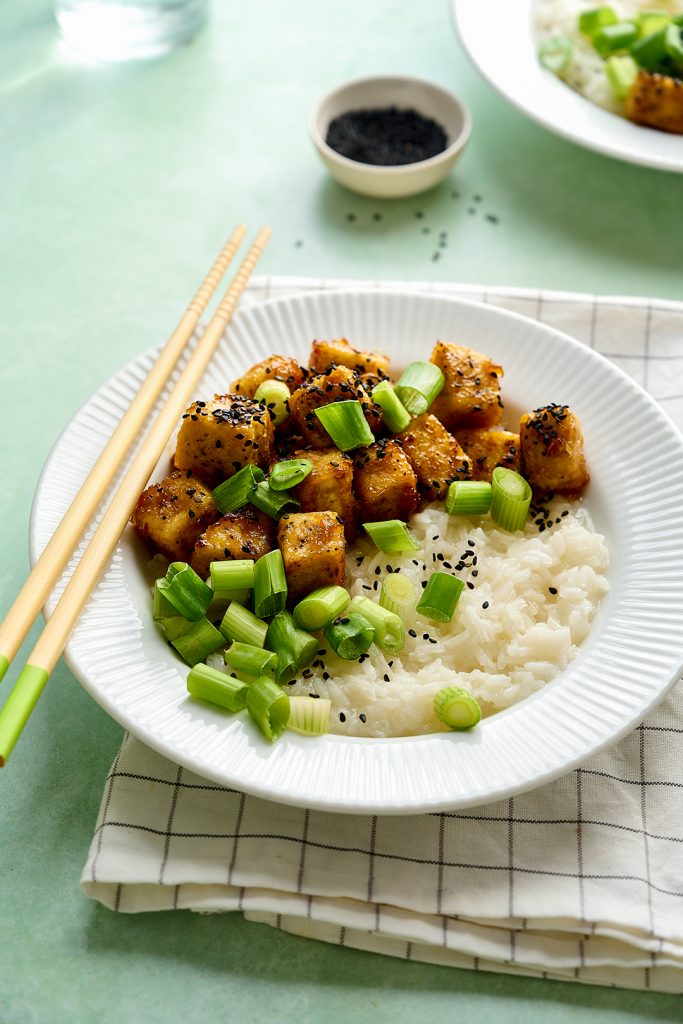 Two bowls of sweet, sticky, ginger tofu on rice with spring onions and black sesame seeds